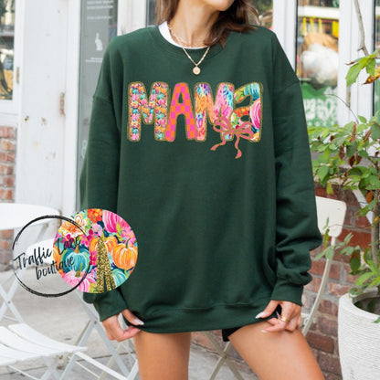 Person wearing a green sweatshirt with colorful 'Mama' design outdoors.